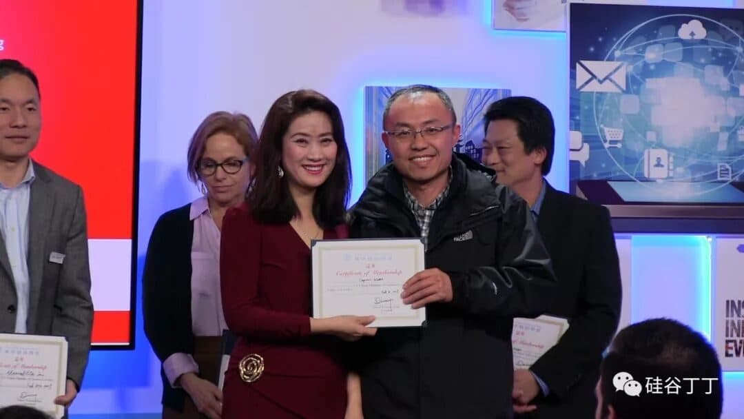 一位身着深红色礼服的女士在台上向获奖者颁发证书,旁边站着其他嘉宾。