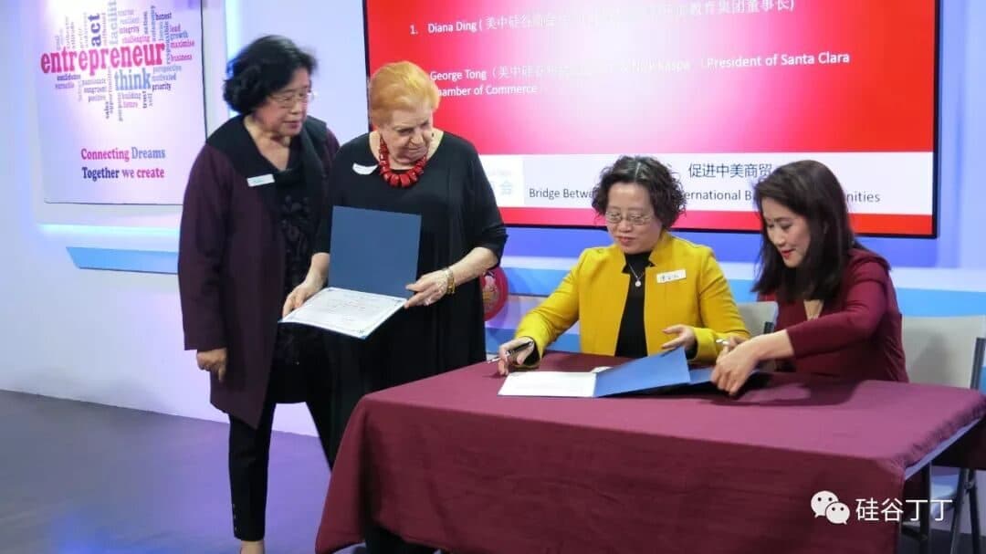 四位代表在铺着台布的签字桌前交换签署文件,身后是投影屏幕。